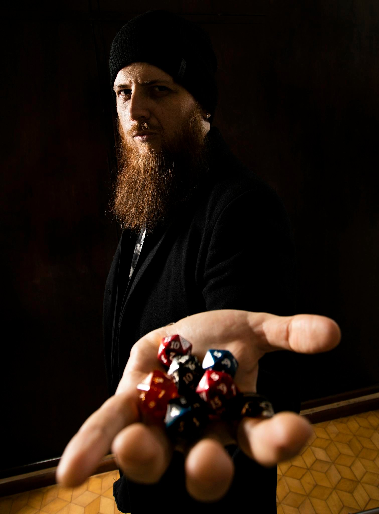 Bearded man presenting colorful dice in a dark, dramatic environment.